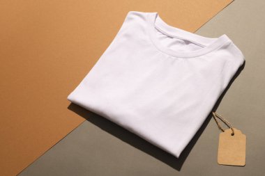 Kahverengi arka planda etiketli beyaz tişörtü kapat ve kopyala. Moda, kıyafetler, renk ve kumaş konsepti.
