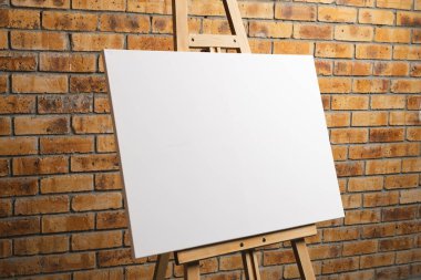 Ahşap sehpadaki beyaz tuval ve tuğla duvar zeminindeki boşluğu kopyala. İmza, yazma alanı ve reklam kavramı.