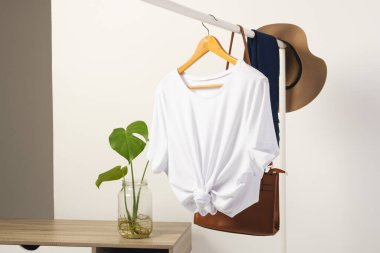 Beyaz tişört, şapka ve kahverengi çanta beyaz arka planda fotokopi alanı olan korkuluklardan sarkıyor. Moda, kıyafetler, renk ve kumaş konsepti.