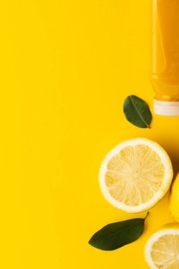 Meyve suyu, limon, limon dilimleri ve sarı arka planda kopya alanı olan yapraklarla şişeyi kapat. Meyve, yemek, tazelik ve renk kavramı.