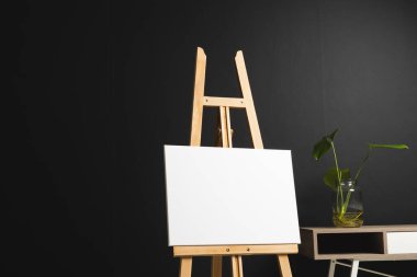 Ahşap sehpada beyaz tuval ve siyah arka planda masa ve bitki örtüsü. İmza, yazma alanı ve reklam kavramı.