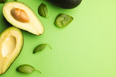 Avokado ve fesleğen yapraklarından oluşan iki yarıyı kapat ve yeşil arka plandaki boşluğu kopyala. Sebze, yiyecek, tazelik ve renk konsepti.