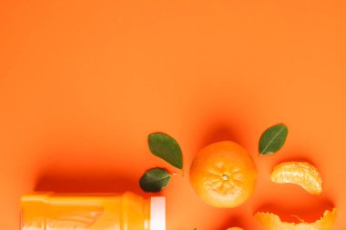 Meyve suyu, mandalina, segmentler ve turuncu arka planda kopya alanı olan yapraklarla şişeyi kapat. Meyve, yemek, tazelik ve renk kavramı.