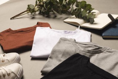 Çok renkli tişörtler, ayakkabılar ve arka planda fotokopi alanı olan not defterleri. Moda, kıyafetler, renk ve kumaş konsepti.