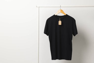 Siyah tişörtlü, etiketli, beyaz arka planda fotokopi alanı olan bir elbise askısı. Moda, kıyafetler, renk ve kumaş konsepti.