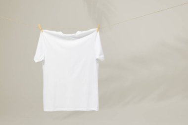 Mandallı çamaşır ipine asılı beyaz tişört ve gri arka planda fotokopi alanı. Moda, kıyafetler, renk ve kumaş konsepti.