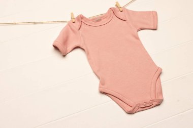 Pembe bebek, beyaz arka planda fotokopi alanı olan askılarla büyür. Bebek modası, kıyafetler, renk ve kumaş konsepti.