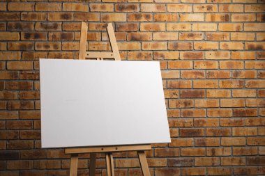 Ahşap sehpadaki beyaz tuval ve tuğla duvar zeminindeki boşluğu kopyala. İmza, yazma alanı ve reklam kavramı.