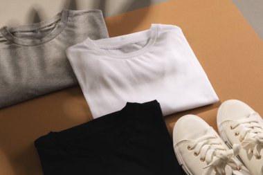 Katlanmış tişörtleri, beyaz spor ayakkabıları ve kahverengi arka plandaki fotokopi alanlarını kapatın. Moda, kıyafetler, renk ve kumaş konsepti.