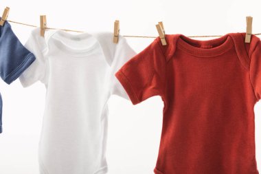 Mandallı çamaşır ipinden sarkan ve beyaz arka planda fotokopi alanı olan üç bebek büyüyor. Bebek modası, kıyafetler, renk ve kumaş konsepti.