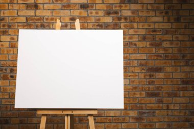 Ahşap sehpadaki beyaz tuval ve tuğla duvar zeminindeki boşluğu kopyala. İmza, yazma alanı ve reklam kavramı.
