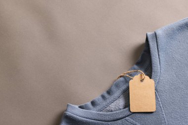 Üzerinde etiket olan mavi tişörtü kapat ve kahverengi arkaplanı kopyala. Moda, kıyafetler, renk ve kumaş konsepti.