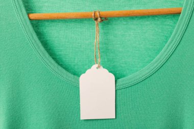 Askıda etiketi olan yeşil tişört ve beyaz arka planda fotokopi alanı. Moda, kıyafetler, renk ve kumaş konsepti.
