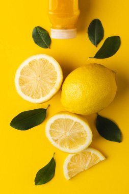 Meyve suyu, limon, limon dilimleri ve sarı arka planda kopya alanı olan yapraklarla şişeyi kapat. Meyve, yemek, tazelik ve renk kavramı.