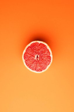 Kırmızı greyfurtun yarısını kapat ve turuncu arka plandaki boşluğu kopyala. Meyve, yemek, tazelik ve renk kavramı.