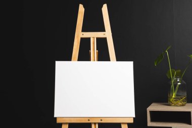 Ahşap sehpada beyaz tuval ve siyah arka planda masa ve bitki örtüsü. İmza, yazma alanı ve reklam kavramı.