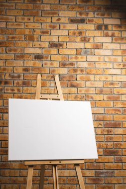 Ahşap sehpadaki beyaz tuval ve tuğla duvar zeminindeki boşluğu kopyala. İmza, yazma alanı ve reklam kavramı.
