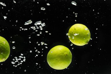 Siyah arka planda kopya alanı olan limonların suya düşüşünü kapat. Meyve, yemek, tazelik ve renk kavramı.