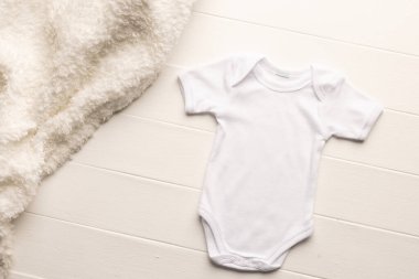 Beyaz bebek beşiği ve beyaz tahta arka planda fotokopi alanı olan kürk halı. Bebek modası, kıyafetler, renk ve kumaş konsepti.