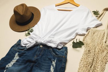 Düz beyaz tişört, güneş şapkası, net çanta ve krema arka planında fotokopi alanı olan kot etek. Moda, kıyafetler, renk ve kumaş konsepti.