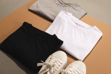 Katlanmış tişörtleri, beyaz spor ayakkabıları ve kahverengi arka plandaki fotokopi alanlarını kapatın. Moda, kıyafetler, renk ve kumaş konsepti.