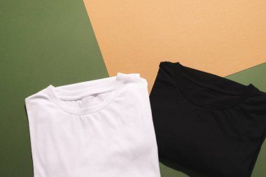 Katlanmış beyaz ve siyah tişörtleri kapatın ve yeşil ile turuncu arkaplanı kopyalayın. Moda, kıyafetler, renk ve kumaş konsepti.