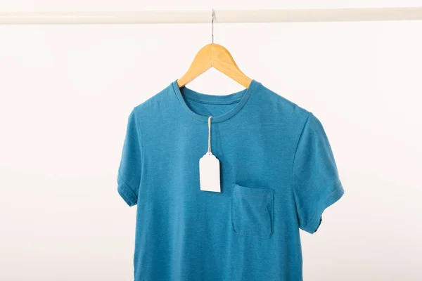 蓝色T恤 衣架上有标签 挂在衣架上 白色背景上有复制空间 色彩和面料概念 — 图库照片