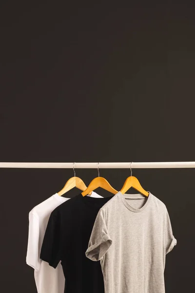 挂在衣架上的三件T恤衫挂在衣架上 在黑色背景上复制空间 色彩和面料概念 — 图库照片