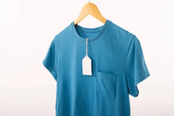 ホワイトバックグラウンドのコピースペースを持つハンガーのタグ付きブルーTシャツ ファッション ファブリックコンセプト — ストック写真