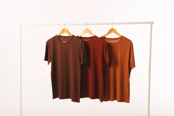 三件棕色T恤衫挂在衣架上 在白色背景上复制空间 色彩和面料概念 — 图库照片
