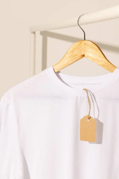 白いTシャツは白い背景のコピースペースが付いている衣服の棚から掛かるタグが付いています ファッション ファブリックコンセプト — ストック写真