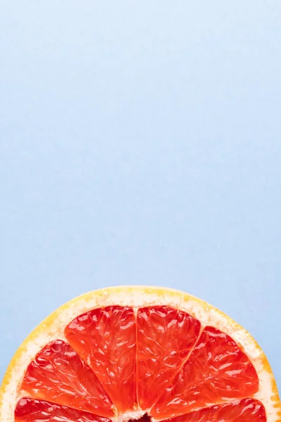 Close up of half of red grapefruit and copy space on blue background. Fruit, food, freshness and colour concept.