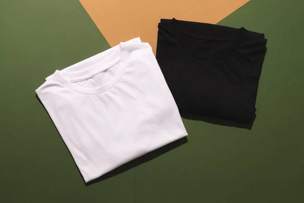 Close up of folded white and black t shirts and copy space on green to orange background. Fashion, clothes, colour and fabric concept.