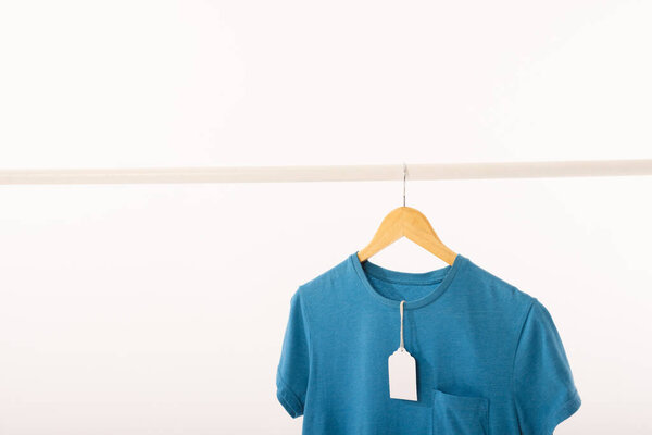 Blue t shirt with tag on hanger hanging from clothes rail with copy space on white background. Fashion, clothes, colour and fabric concept.
