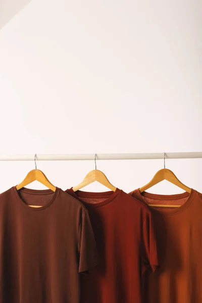 衣服の柵から掛かるハンガーの3つの茶色のTシャツおよび白い背景のスペースをコピーして下さい ファッション ファブリックコンセプト — ストック写真