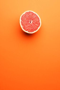 Kırmızı greyfurtun yarısını kapat ve turuncu arka plandaki boşluğu kopyala. Meyve, yemek, tazelik ve renk kavramı.