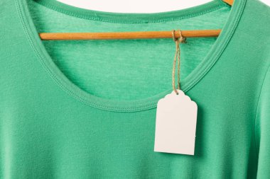 Askıda etiketi olan yeşil tişört ve beyaz arka planda fotokopi alanı. Moda, kıyafetler, renk ve kumaş konsepti.