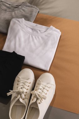 Katlanmış tişörtleri, beyaz spor ayakkabıları ve kahverengi arka plandaki fotokopi alanlarını kapatın. Moda, kıyafetler, renk ve kumaş konsepti.