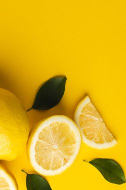 Limon, limon dilimleri ve sarı arka planda fotokopi alanı olan yapraklar. Meyve, yemek, tazelik ve renk kavramı.