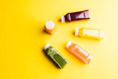 Plastik şişeleri taze meyve suyu ile kapatın ve sarı arka planda kopya alanı oluşturun. Meyve, içecek, yiyecek, tazelik ve renk kavramı.