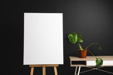 Ahşap sehpada beyaz tuval ve siyah arka planda masa ve bitki örtüsü. İmza, yazma alanı ve reklam kavramı.