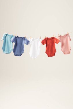 Mandallı çamaşır ipinden sarkan çok renkli bebekler ve beyaz arka planda fotokopi alanı. Bebek modası, kıyafetler, renk ve kumaş konsepti.