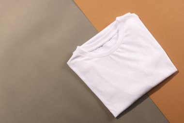 Katlanmış beyaz t-shirtleri kapatın ve kahverengi arkaplandaki boşluğu kopyalayın. Moda, kıyafetler, renk ve kumaş konsepti.