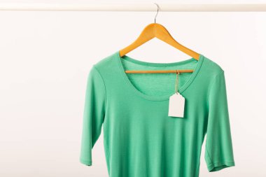 Askıda asılı yeşil tişört, beyaz arka planda fotokopi alanı var. Moda, kıyafetler, renk ve kumaş konsepti.