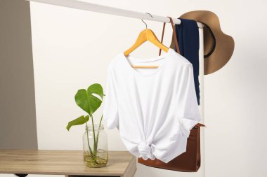 Beyaz tişört, şapka ve kahverengi çanta beyaz arka planda fotokopi alanı olan korkuluklardan sarkıyor. Moda, kıyafetler, renk ve kumaş konsepti.