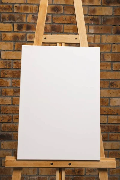 木製のイーゼルに白いキャンバスがあり レンガの壁の背景にスペースをコピーします サイネージ ライティングスペース 広告コンセプト — ストック写真