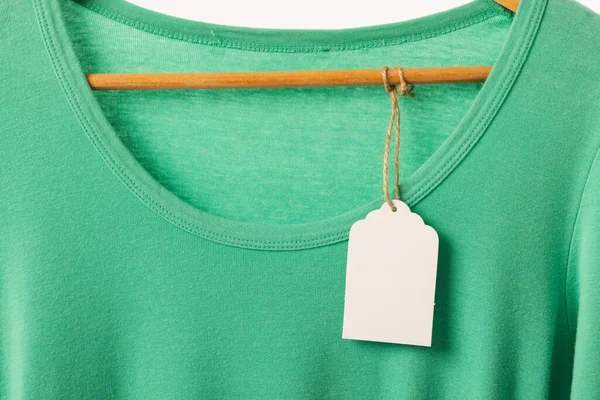 Askıda etiketi olan yeşil tişört ve beyaz arka planda fotokopi alanı. Moda, kıyafetler, renk ve kumaş konsepti.