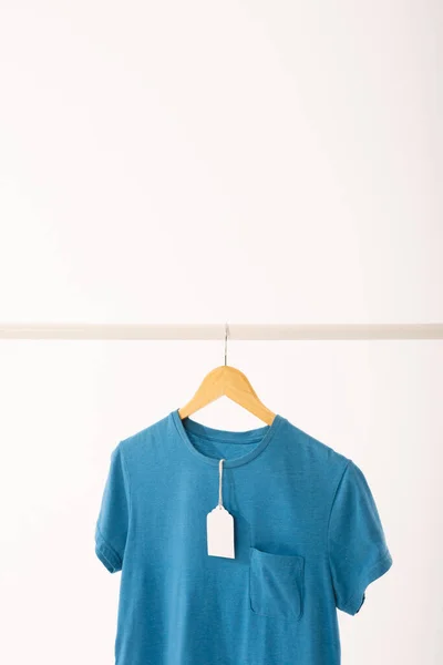 배경에 공간이있는 레일에서 걸이에 태그가있는 파란색 티셔츠 — 스톡 사진