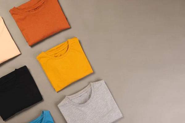 Multi coloured t shirts with copy space on grey floor background. Fashion, clothes, colour and fabric concept.