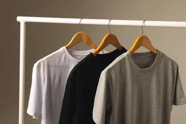 衣服の柵から掛かるハンガーの3つのTシャツおよび灰色の背景のスペースをコピーして下さい ファッション ファブリックコンセプト — ストック写真